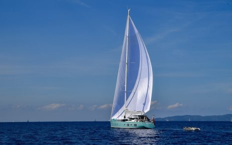 A sailing yacht with a large white sail gliding over calm blue waters under a clear sky