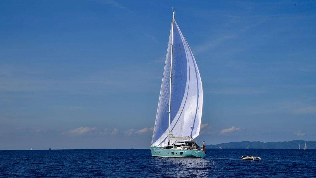 A sailing yacht with a large white sail gliding over calm blue waters under a clear sky